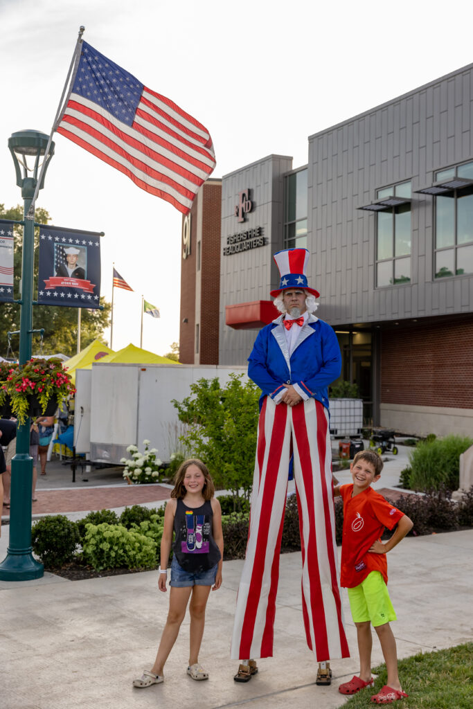man dressed patriotically on stilts posing by child