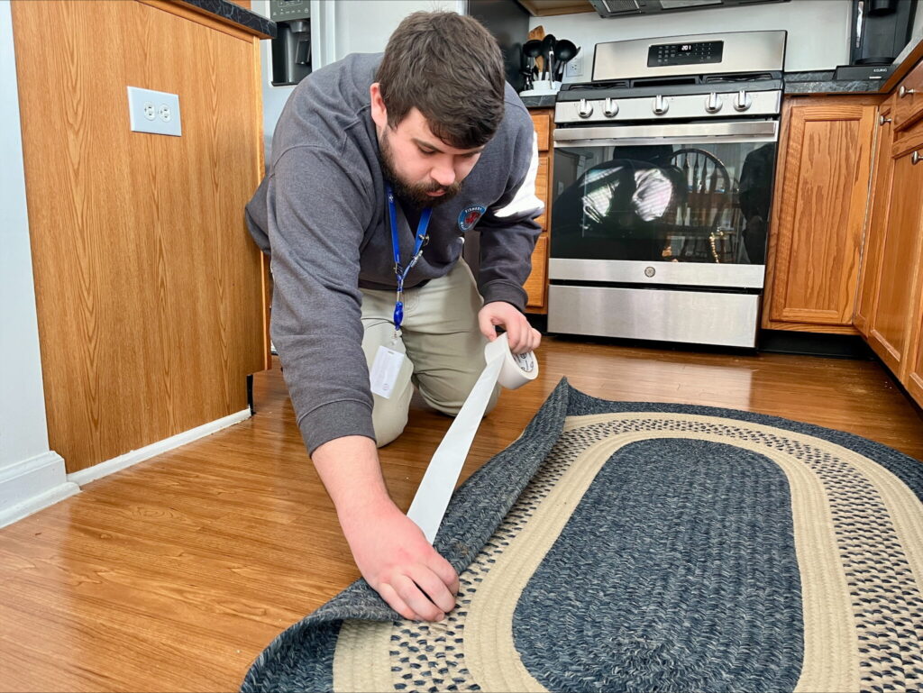 fallprevent man putting down tape on a rug to prevent falls